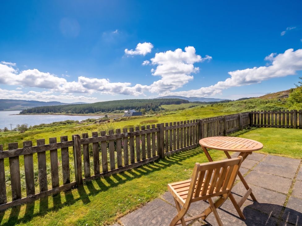 A patio with a table and chair overlooking the landscape at Poppies Cottage, Craignure, Isle Of Mull