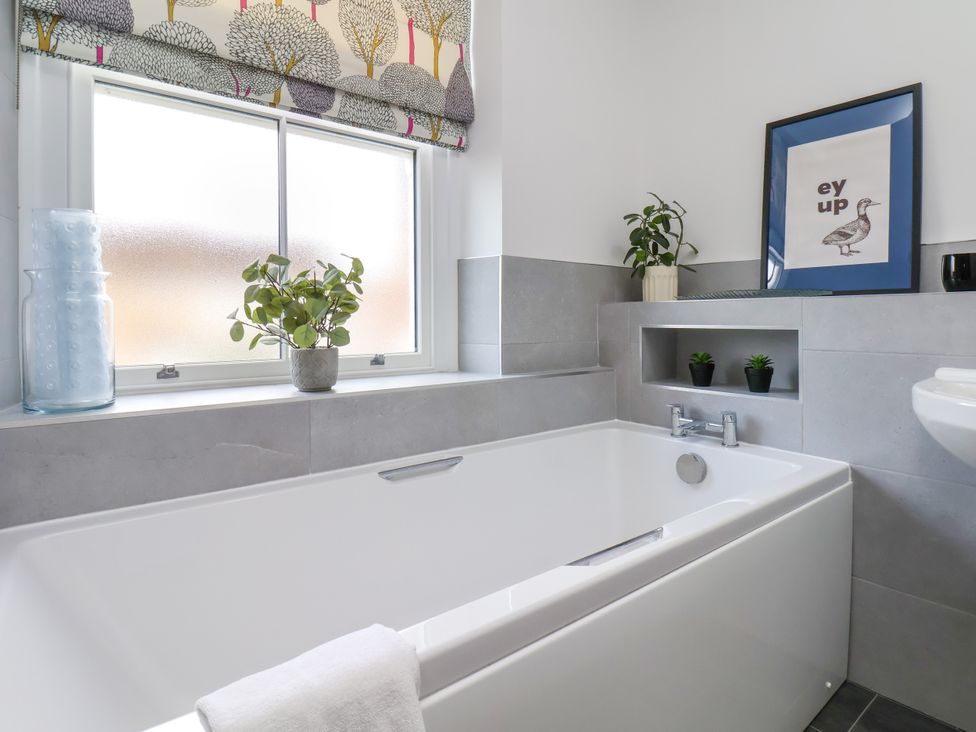 A bathroom with a bathtub, plants, and a window at 1 Roxby Terrace in Thornton-le-Dale