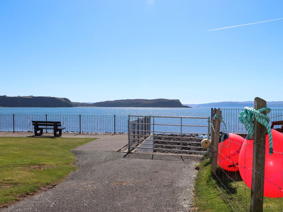 An outdoor area by the water with a bench and a gate at Ceól na Mara Uig