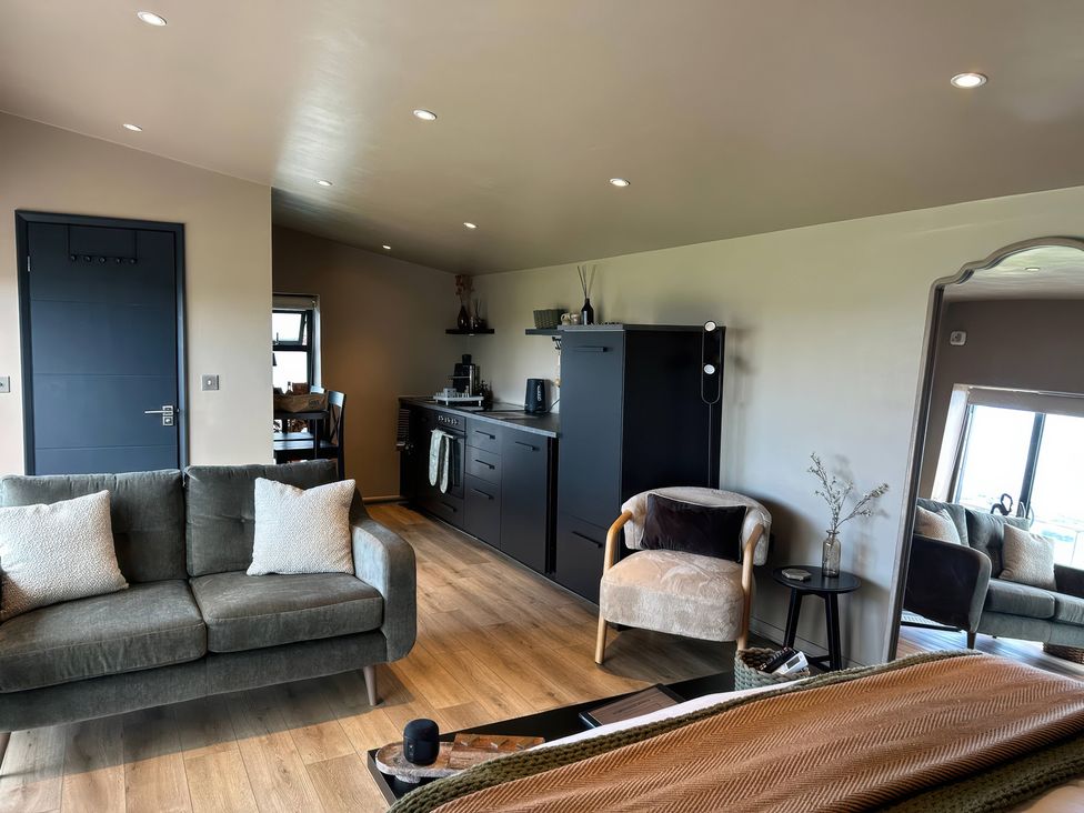 A living room with a sofa, armchair, and kitchen area at Heath Hideaway in Norland near Ripponden