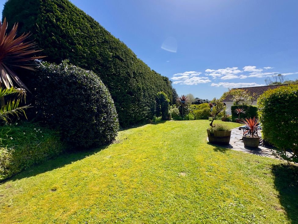 A garden with grass, hedges, and planters at Kilcarreg in Rock near Wadebridge
