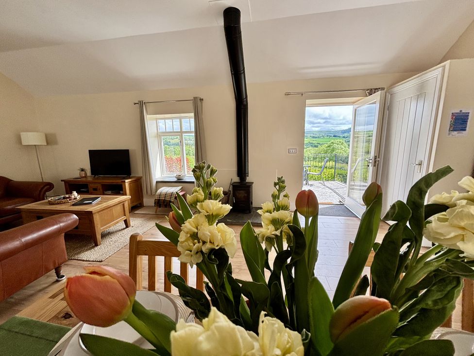 A living room with a sofa, television, and door to the outside at Llaethdy - The Dairy in Boncath near Crymych