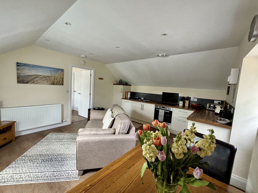 A living room with a sofa and flowers on a table at Lloft Gwair - Hayloft Boncath near Crymych
