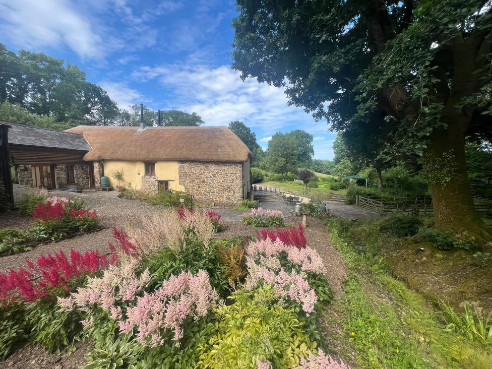 A garden with flowers and a thatched building at The Milking Parlour in Highampton