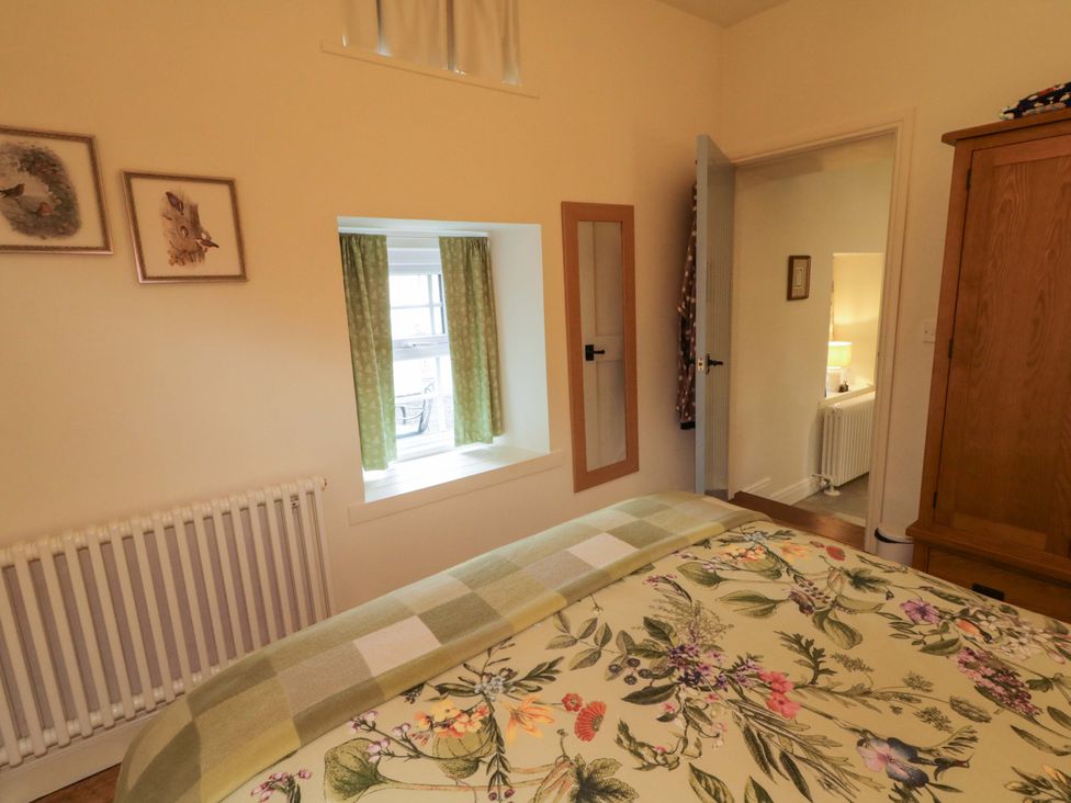 A bedroom with a bed, window, and wooden wardrobe at Rosslare Cottage, Broughshane