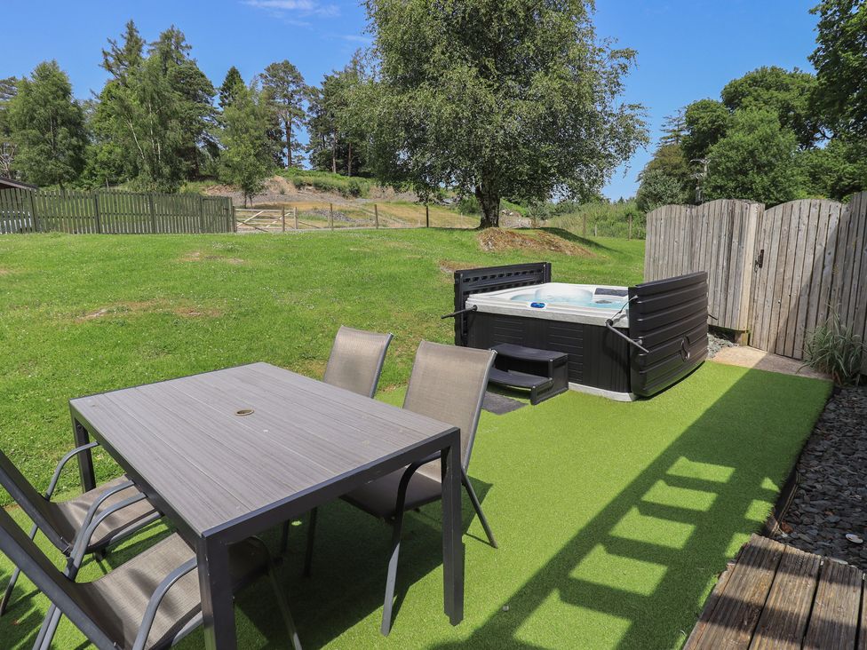 A garden with a table and chairs next to a hot tub at Yew - Woodland Cottages in Bowness-On-Windermere
