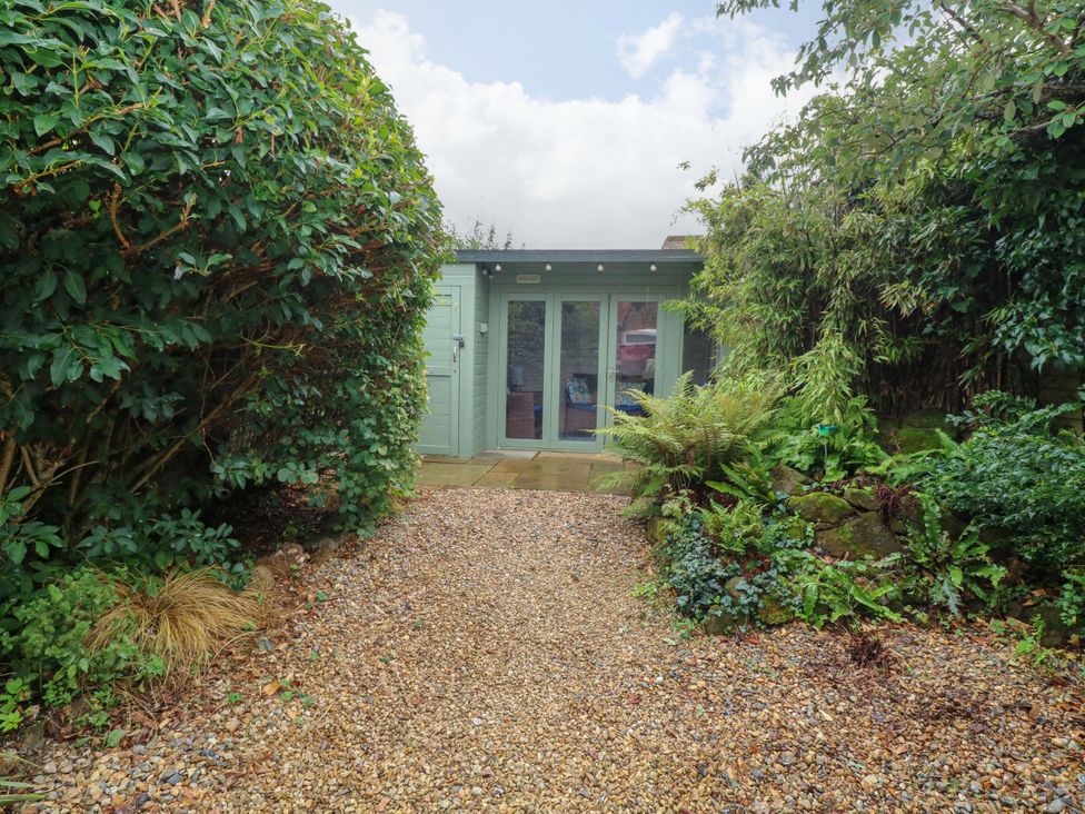 A garden with a gravel path leading to a green door at Fern Cottage in Heacham