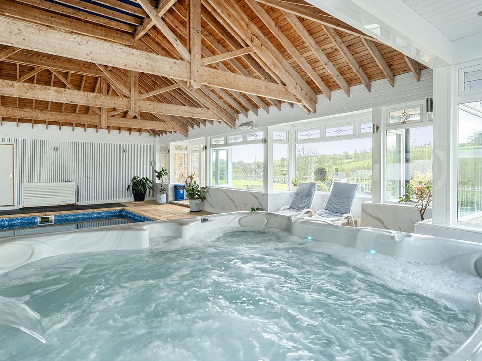 An indoor swimming pool area with a hot tub and seating at Chapel Green Studio Polgooth near St Austell