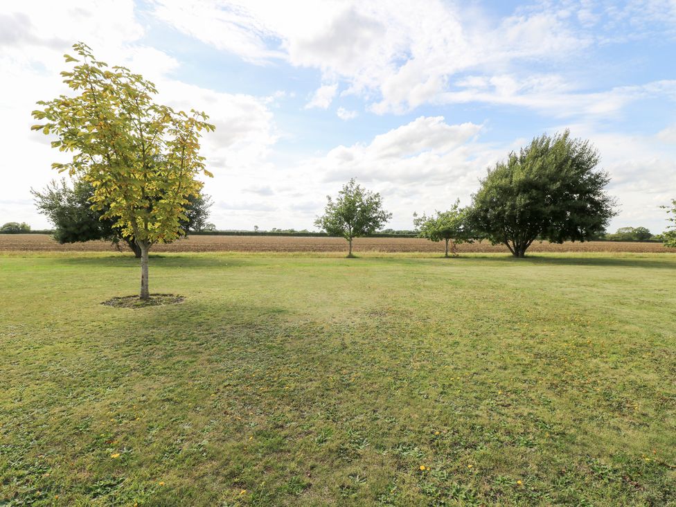 A grassy area with trees and a field at The Annexe in Litcham