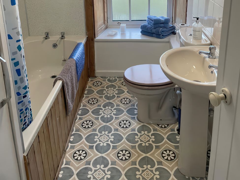 A bathroom with a bath tub, toilet, sink, and towels at The Pink House Isle Of Whithorn
