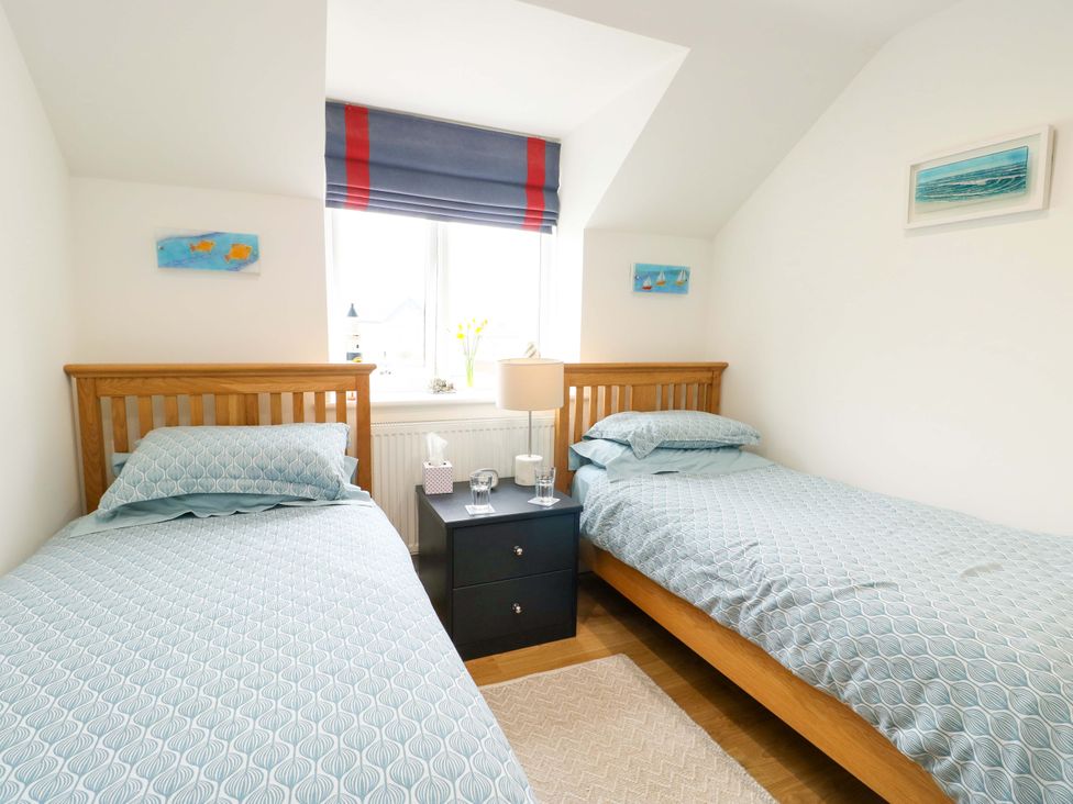 A bedroom with two beds and a nightstand at Maelog, 14 Tides Reach Rhosneigr