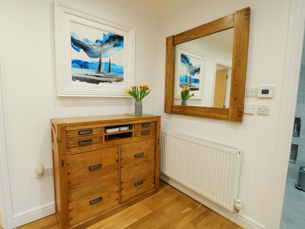 A hallway with a wooden cabinet, mirror, and painting at Maelog, 14 Tides Reach Rhosneigr