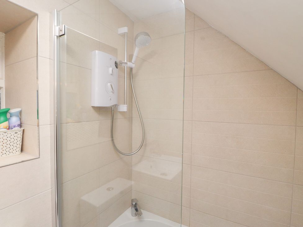 A shower with glass enclosure and tiled walls at Merlin in Llithfaen near Nefyn