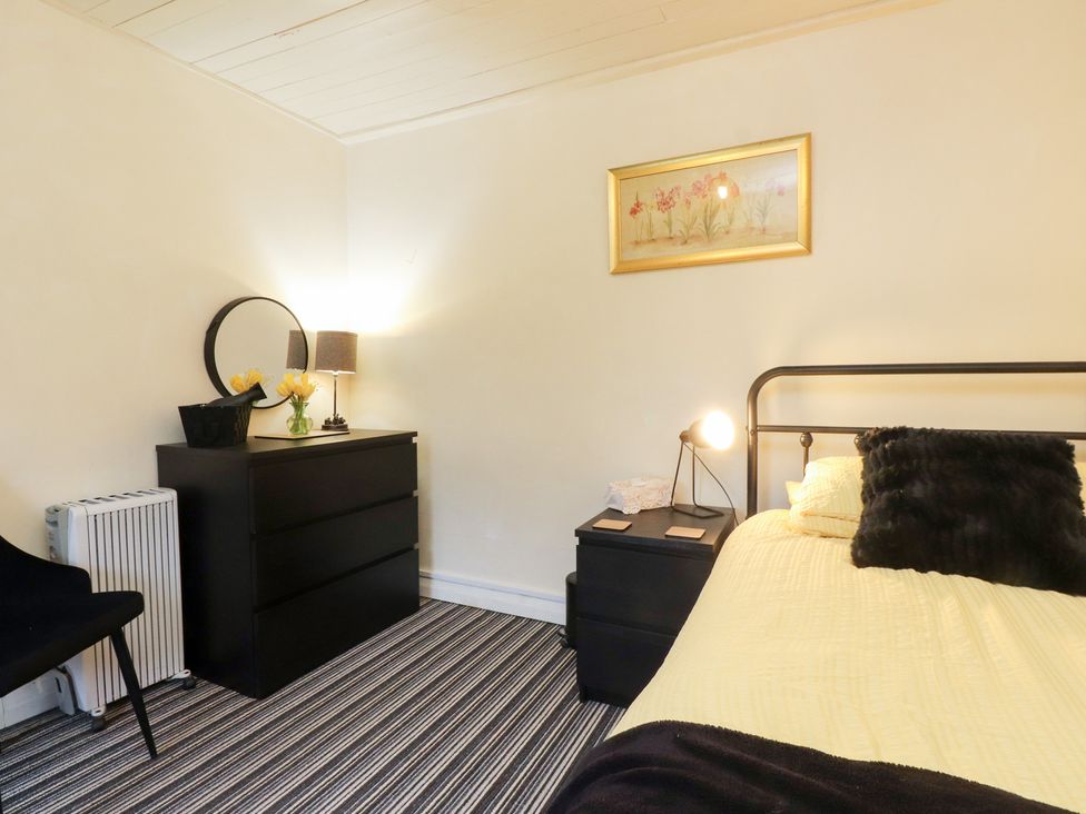 A bedroom with a bed, dresser, and lamp at Merlin in Llithfaen near Nefyn