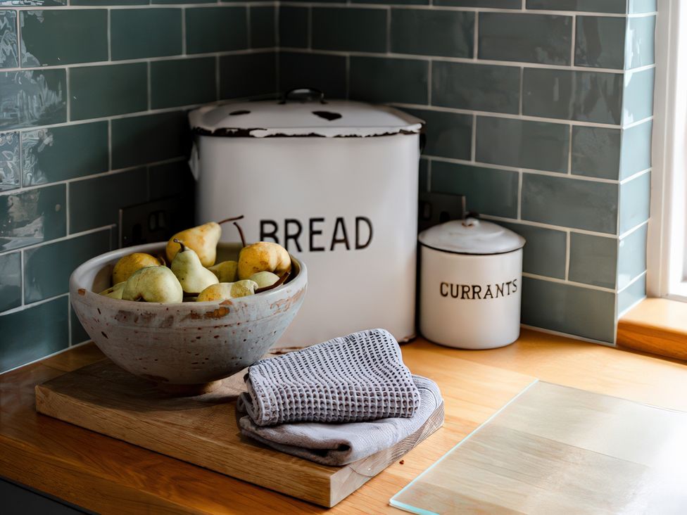 A kitchen counter with a bowl of pears and storage containers at Bridge End Cottage Stainforth
