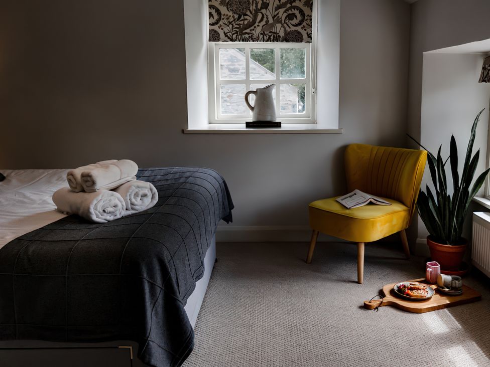 A bedroom with a bed and a yellow armchair at Bridge End Cottage Stainforth