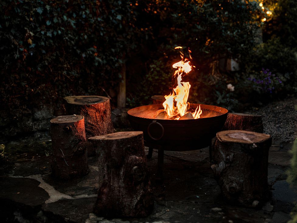 A fire pit surrounded by log seating in a garden at Bridge End Cottage Stainforth