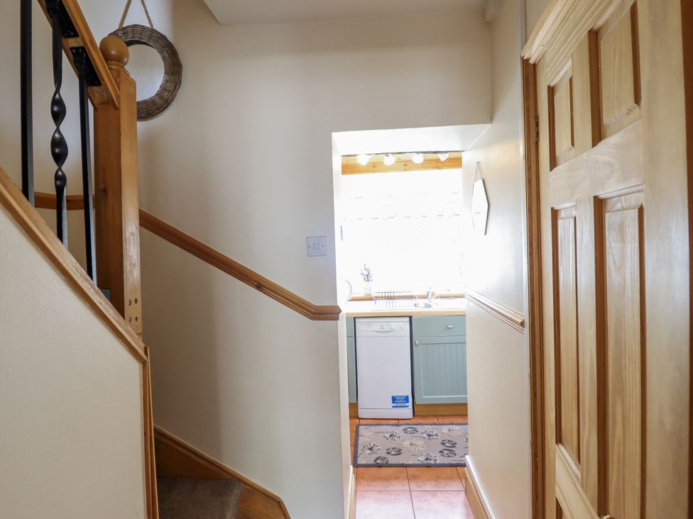 A hallway with a staircase view and kitchen in the background at Cae Tanws Bach, Dolgellau