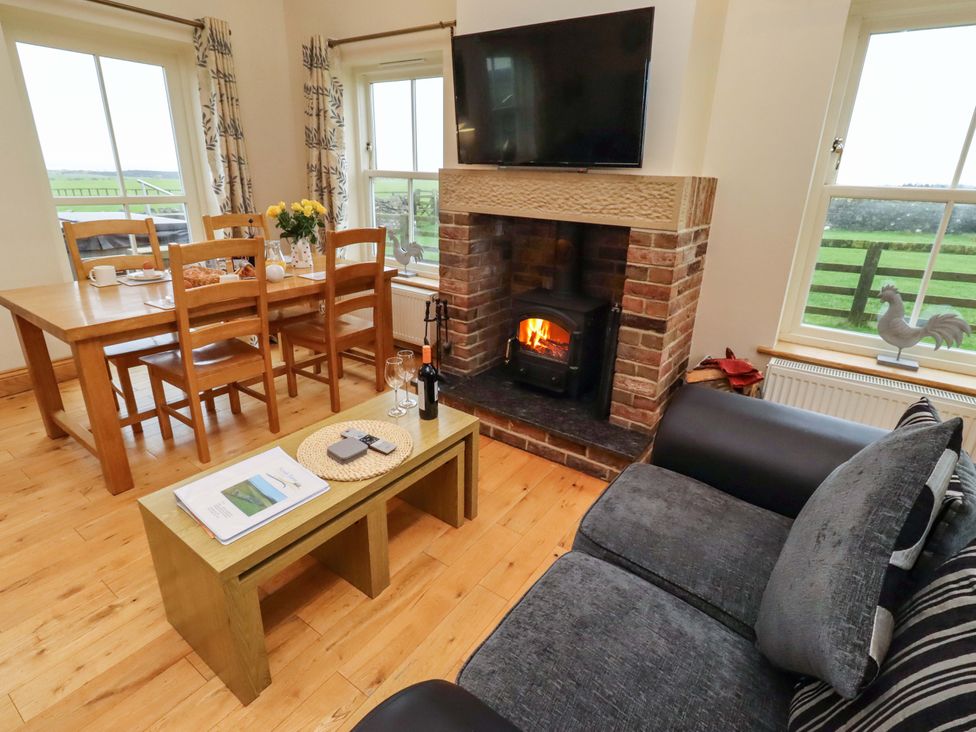 A living room with a fireplace and dining area at Bank Top Cottage in Embleton