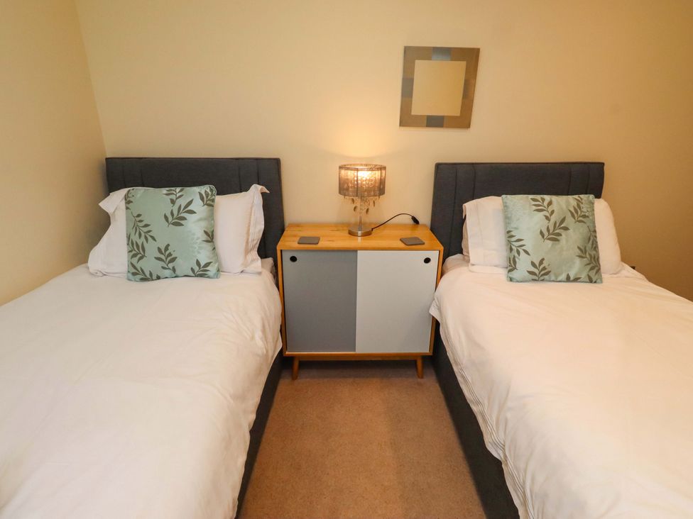 A bedroom with two beds and a nightstand with a lamp at Bank Top Cottage in Embleton