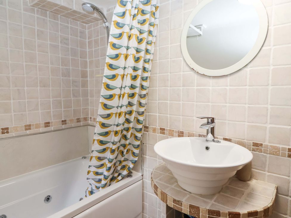 A bathroom with a bathtub, sink, and shower curtain at Clara's Cottage in West Lutton near Malton