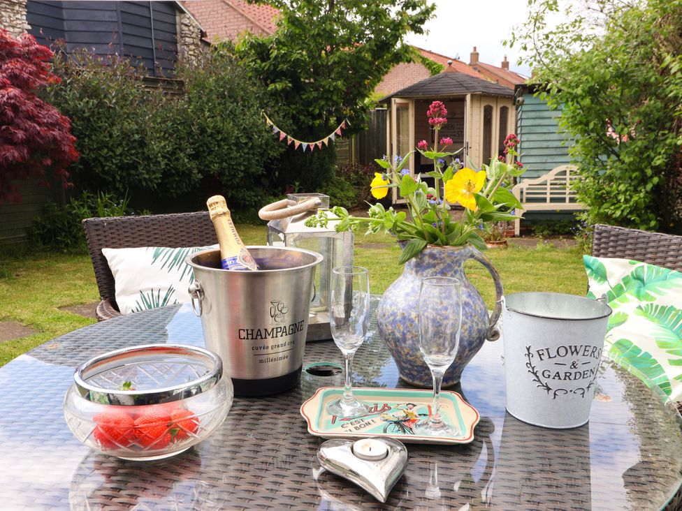A garden table with a champagne bucket, glasses, and a flower vase at Clara's Cottage, West Lutton near Malton