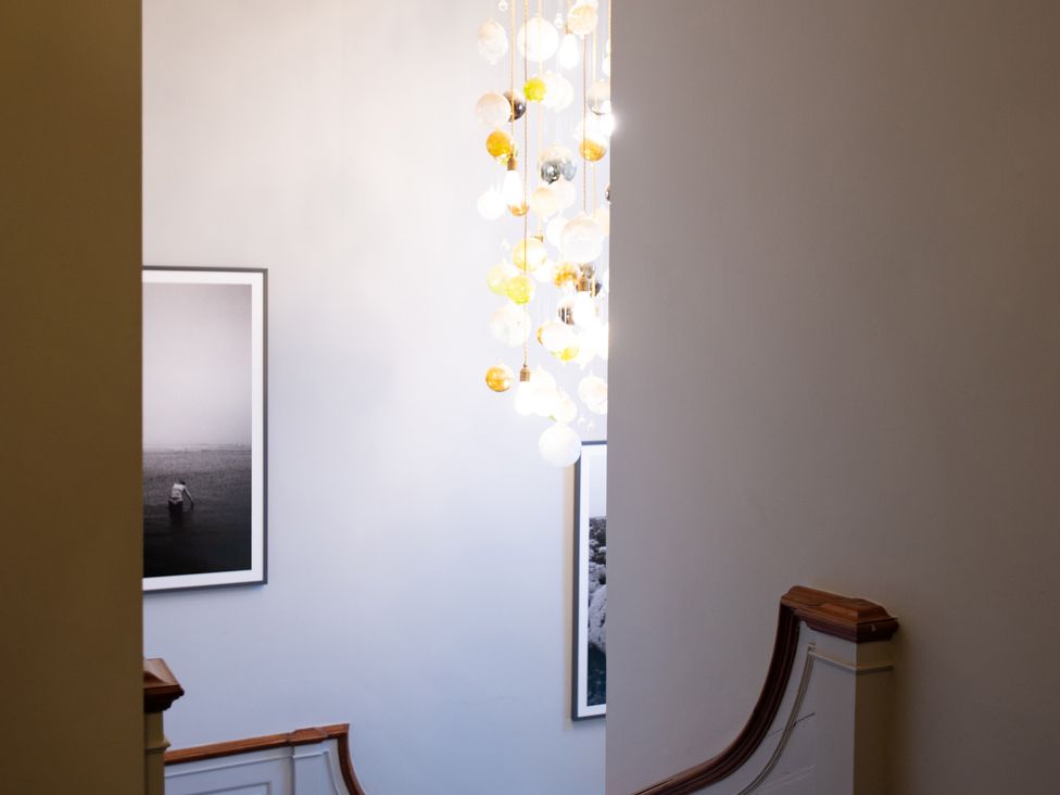 A staircase with a chandelier and framed photographs at Wren Place Hall in Worsbrough