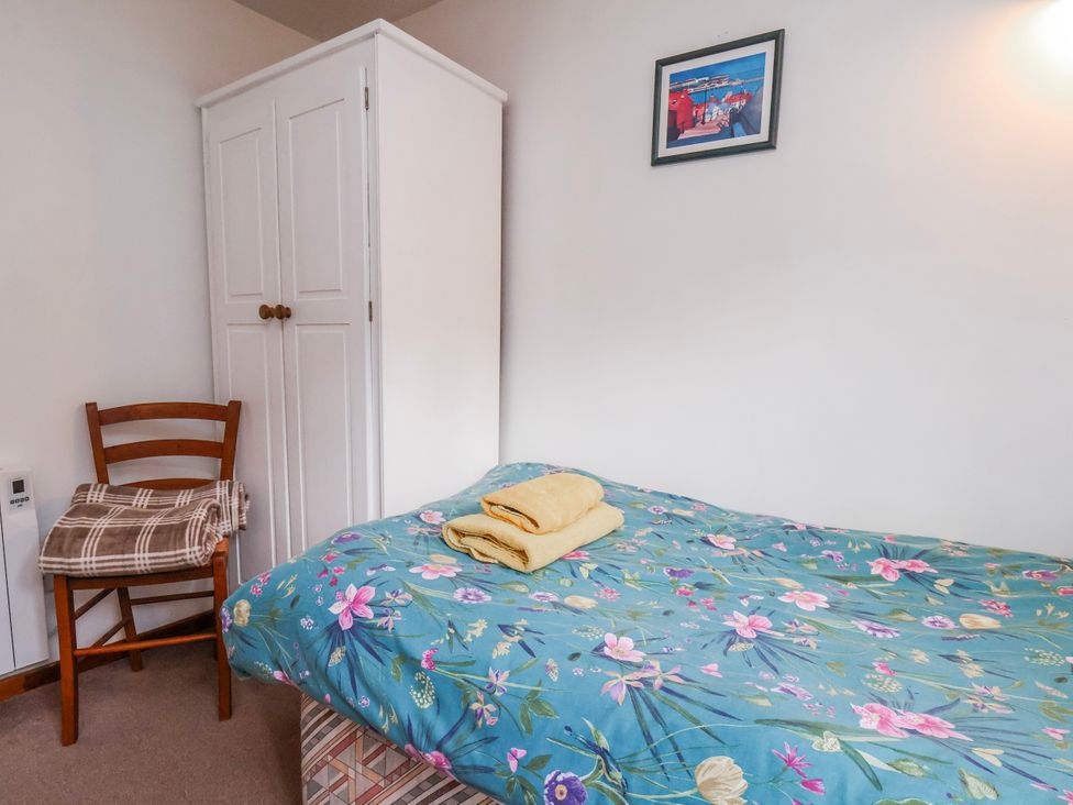 A bedroom with a bed, wardrobe, chair, and towels at Waterside Cottage in Whitby