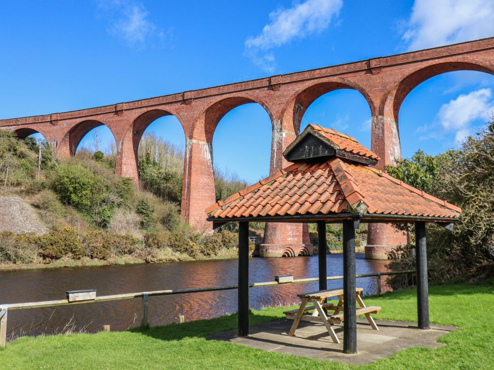 A pavilion with seating beside a river under a viaduct at Waterside Cottage in Whitby