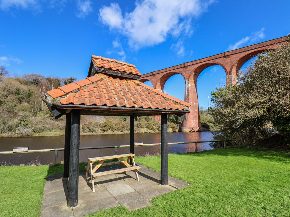A gazebo with a bench near a river and a viaduct at Waterside Cottage in Whitby