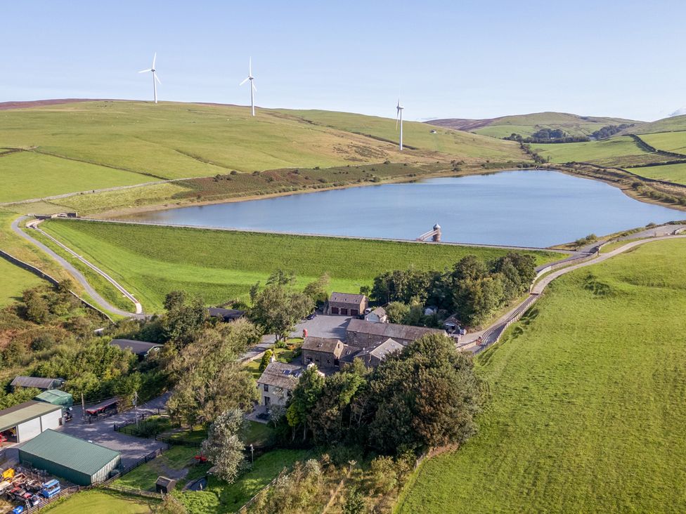 An aerial view of a lake surrounded by fields and wind turbines at Ash Lodge in Pennington near Ulverston