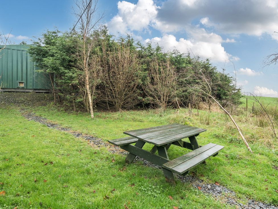 A picnic table on grass with bushes and a container in the background at Ash Lodge near Ulverston