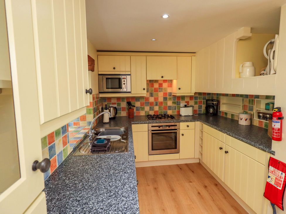 A kitchen with cabinets, stove, sink, and appliances at Pheasant Cottage Beckside near Cartmel