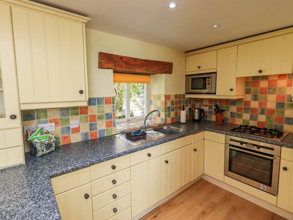 A kitchen with sink, stove and microwave at Pheasant Cottage Beckside near Cartmel
