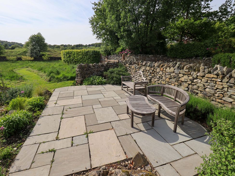 An outdoor seating area with stone patio and wooden furniture at Pheasant Cottage Beckside near Cartmel