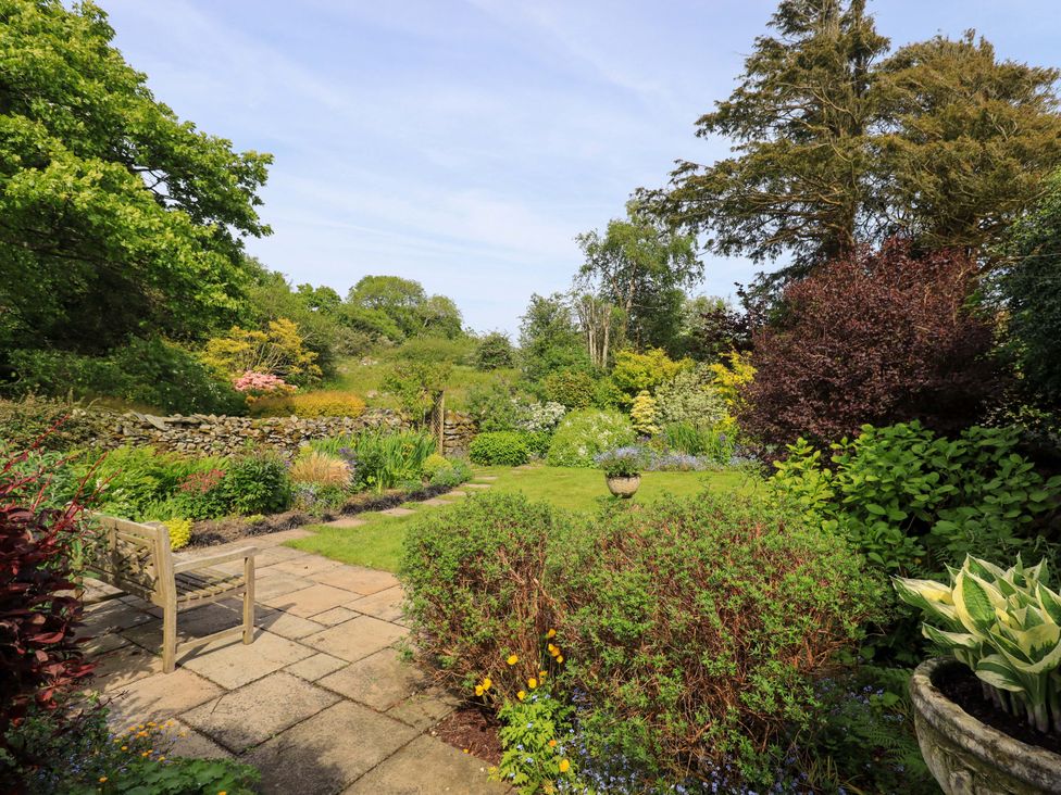 A garden with flowers and a bench at Pheasant Cottage in Beckside near Cartmel