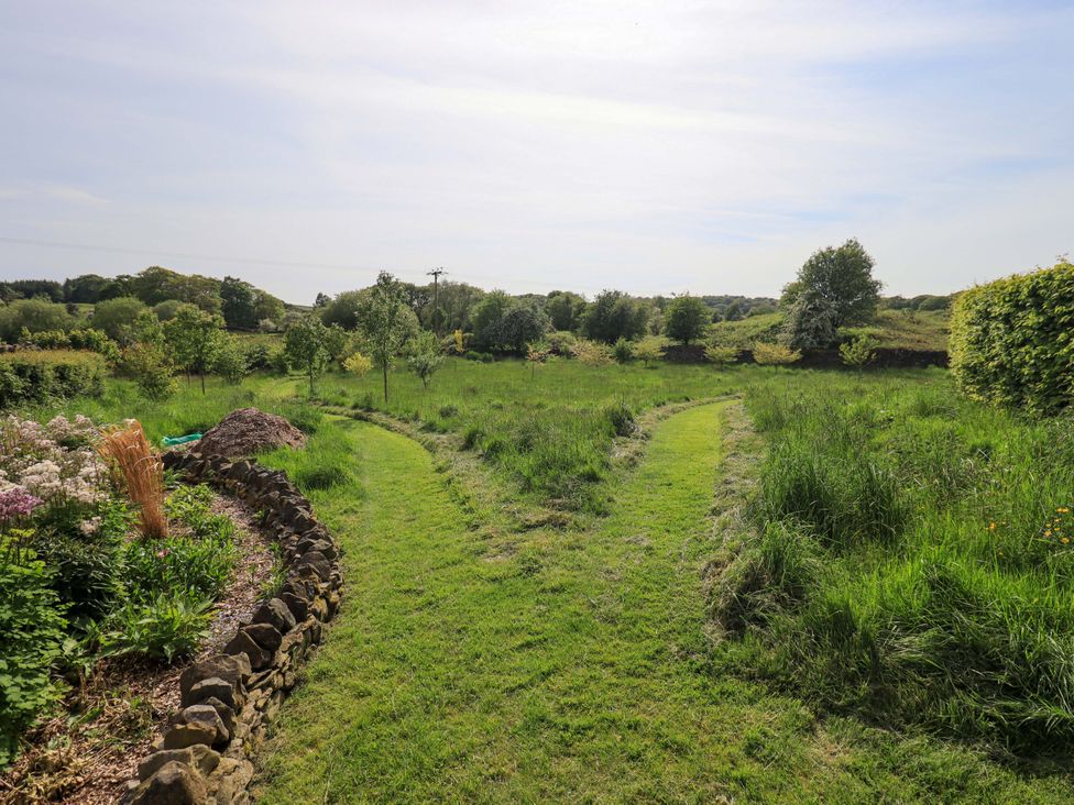 A garden with a winding path and trees at Pheasant Cottage Beckside near Cartmel