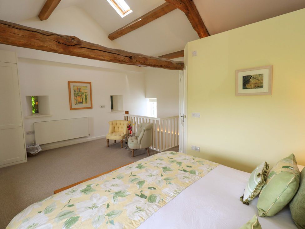 A bedroom with a bed and chair at Kestrel Cottage Beckside near Cartmel