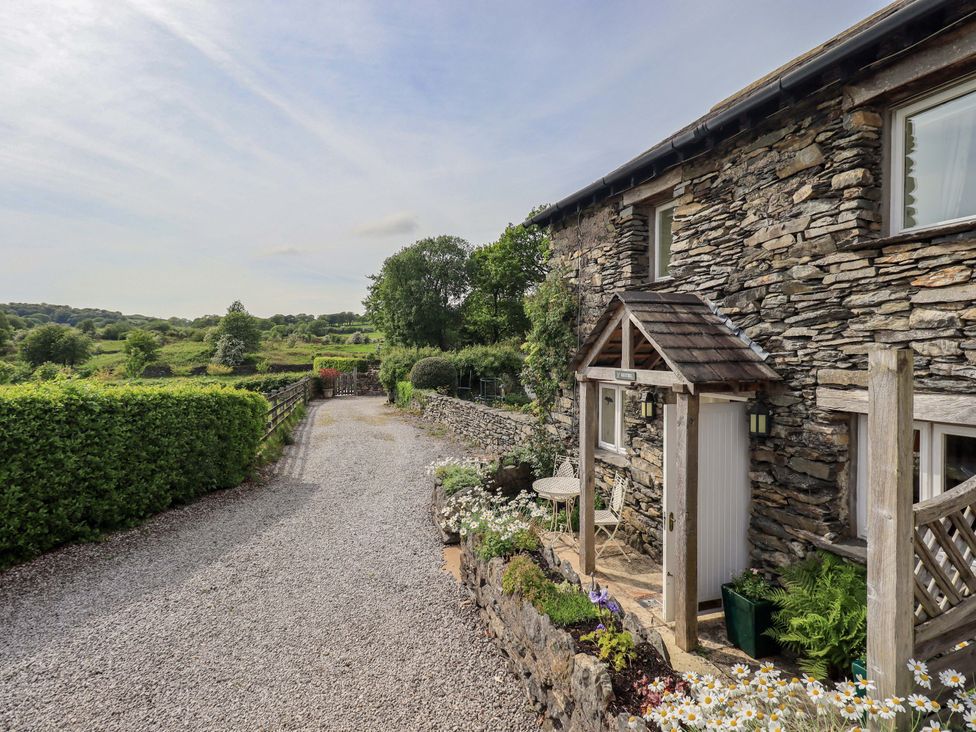 An outdoor view of a stone house with a gravel driveway at Kestrel Cottage near Cartmel