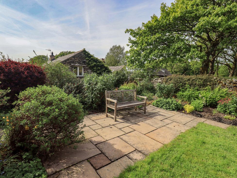 A garden with a stone pathway and a wooden bench at Kestrel Cottage Beckside near Cartmel