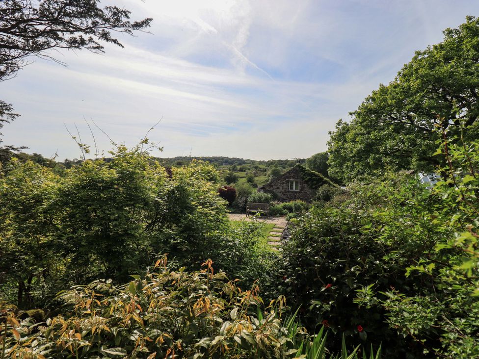 A garden with trees and a stone building in the background at Kestrel Cottage Beckside near Cartmel