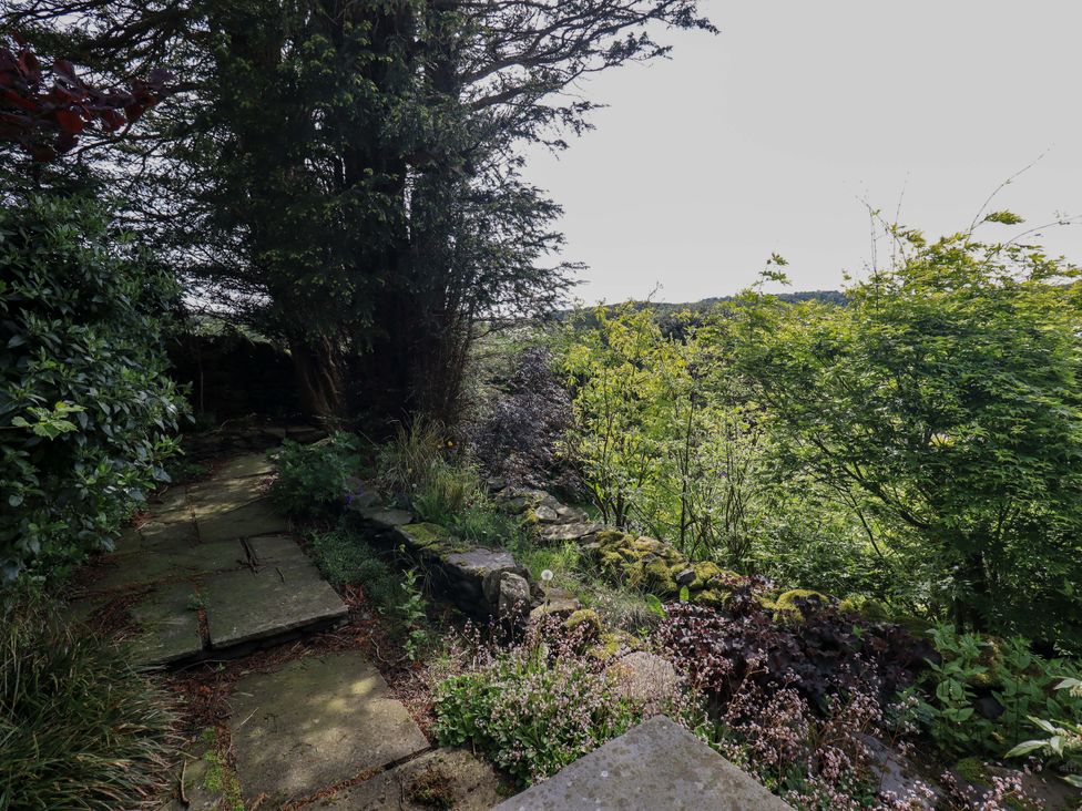 A garden with a stone pathway and trees at Kestrel Cottage in Beckside near Cartmel
