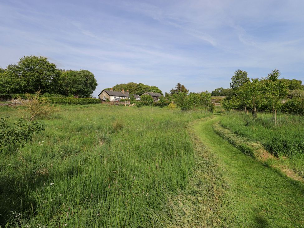 A grassy field with trees and a pathway leading to a house at Kestrel Cottage Beckside near Cartmel