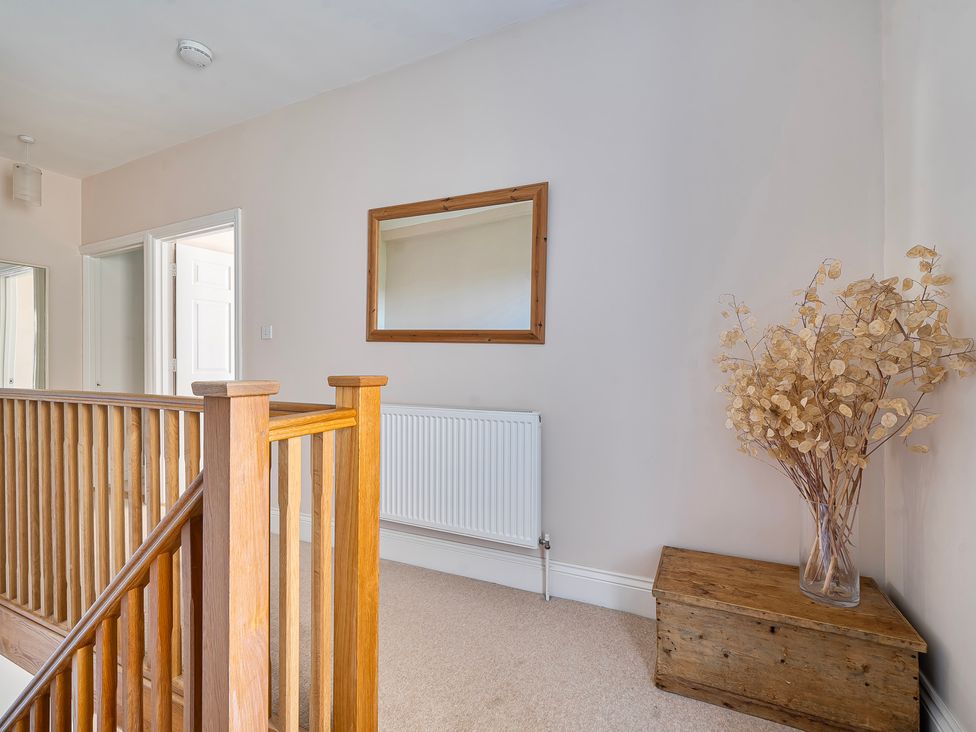 A hallway with a staircase, mirror, radiator, and a decorative plant at East Wing in Crewkerne