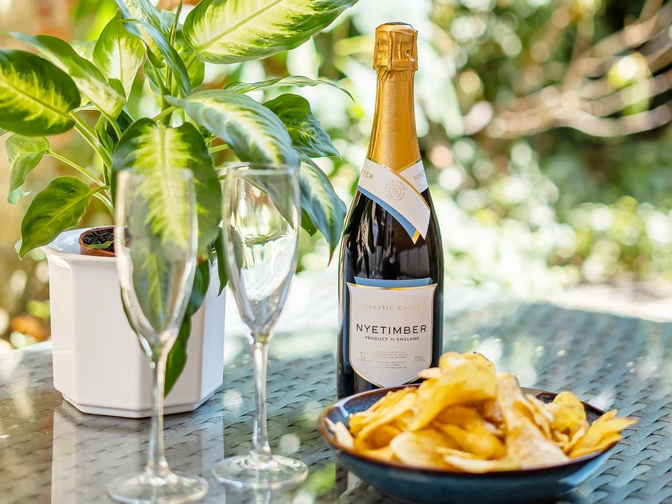 A bottle of Nyetimber with champagne flutes and a bowl of potato chips in a garden setting at East Wing in Crewkerne