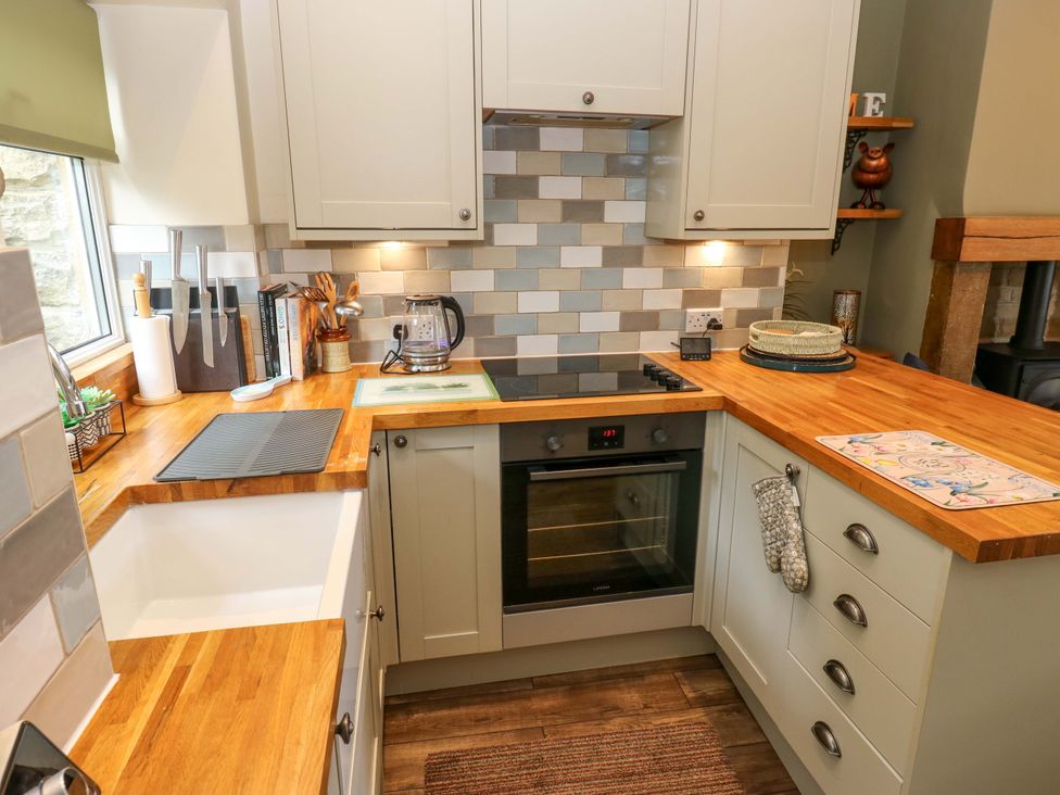 A kitchen with cabinets, sink, stove, and wooden countertop at Maria Cottage in Haworth