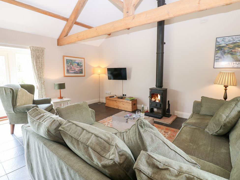 A living room with a sofa, armchair, and wood stove at Shepherds Burn Cottage in Bellingham