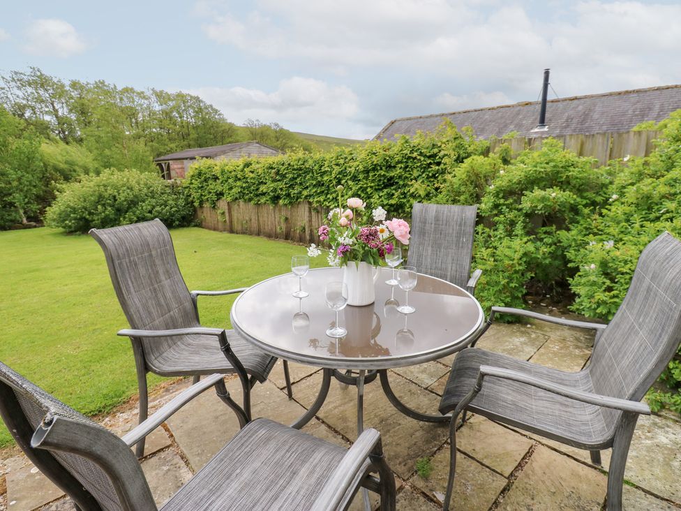 A table with chairs and a vase of flowers in the garden at Shepherds Burn Cottage in Bellingham
