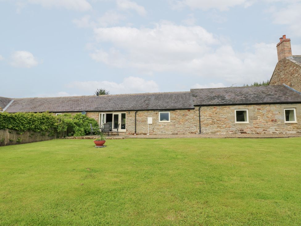 A cottage with a lawn and patio chairs at Shepherds Burn Cottage in Bellingham