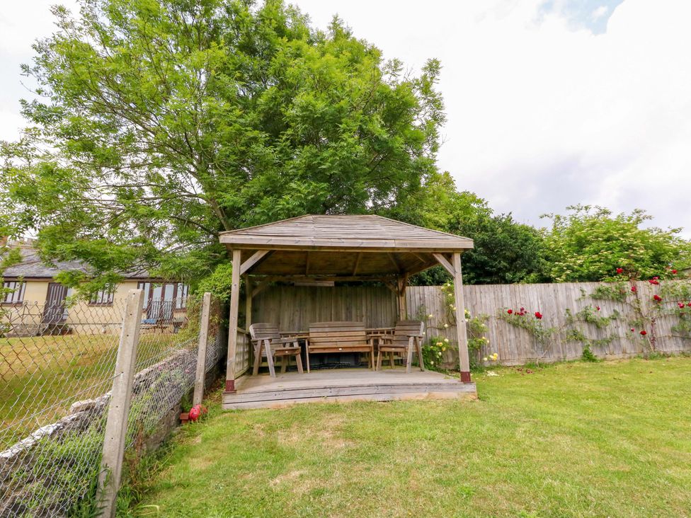 A gazebo with benches and a table in a garden at Mallows Byre in Yetminster